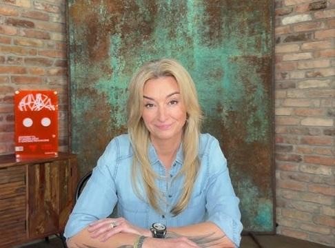Martyna Wojciechowska w stroju podróżniczym na tle egzotycznego krajobrazu, symbolizującym jej podróże i osiągnięcia, takie jak zdobycie szczytów górskich.