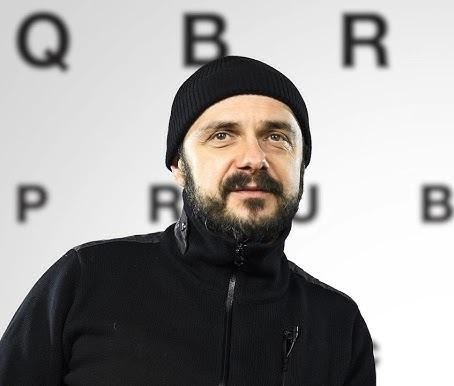 Arkadiusz Jakubik jako wokalista zespołu Dr Misio, śpiewający z pasją na scenie, z mikrofonem w dłoni, w dynamicznym oświetleniu koncertowym.