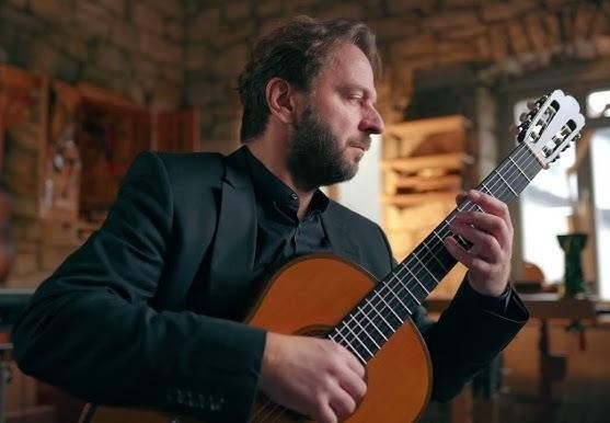 Marcin Dylla w sali lekcyjnej szkoły muzycznej, trzymający gitarę.