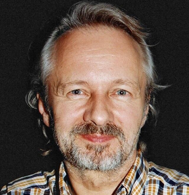 Zbliżenie na klasyczną kamerę filmową lub klaps filmowy, z rozmytym tłem sugerującym plan filmowy lub teatralną scenę.