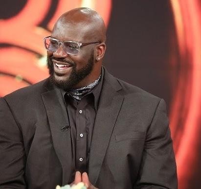 Shaquille O'Neal uśmiechnięty, w swobodnym stroju, w otoczeniu dzieci, symbolizujący jego działalność filantropijną.