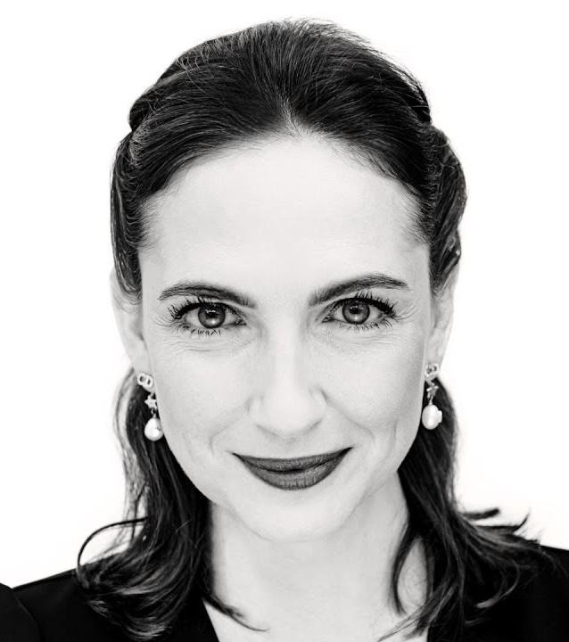 Anna Cieślak z telefonem w dłoni, uśmiechnięta, prawdopodobnie podczas interakcji na Instagramie, z rozmytym tłem sugerującym plan filmowy lub teatralny.