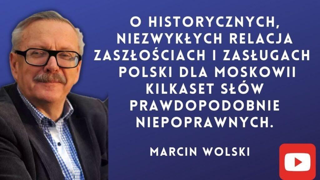 Marcin Wolski w studiu radiowym, dynamiczne ujęcie podczas audycji, z mikrofonem, w tle subtelne elementy studia radiowego.